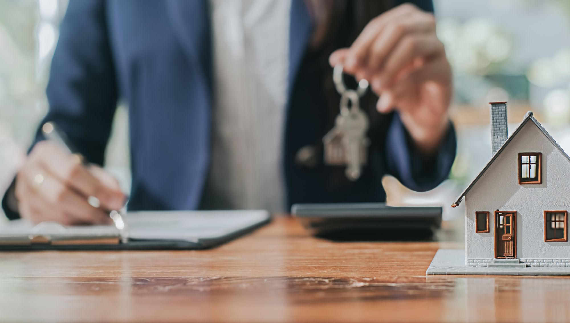 A mortgage consultant handing over house keys while a client signs documents, representing a mortgage consultation program that ensures compliance and smooth home financing.